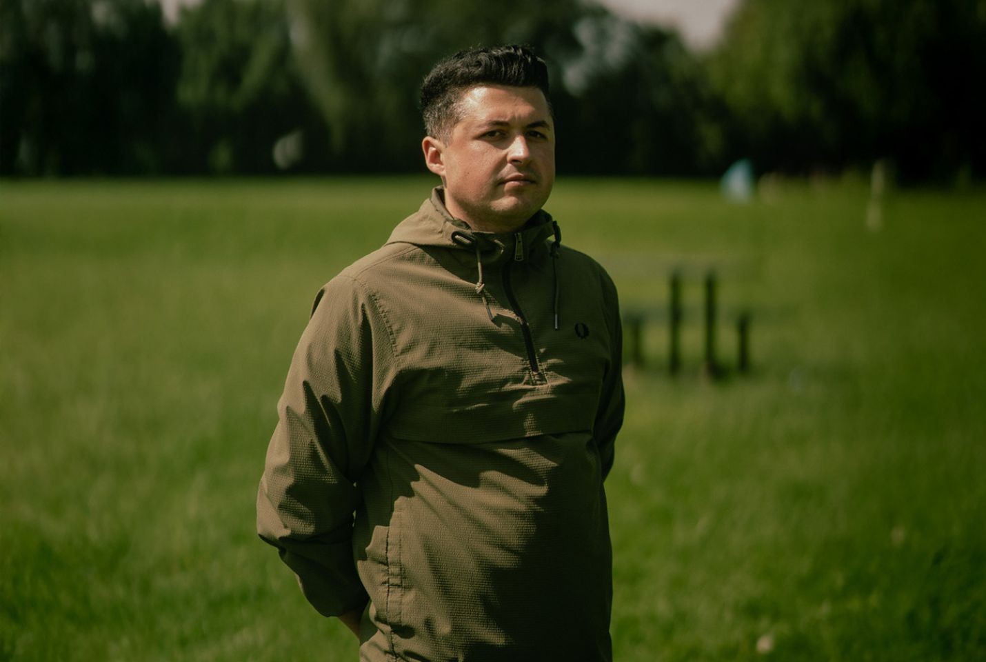A man with dark hair in a green coat stood in a field